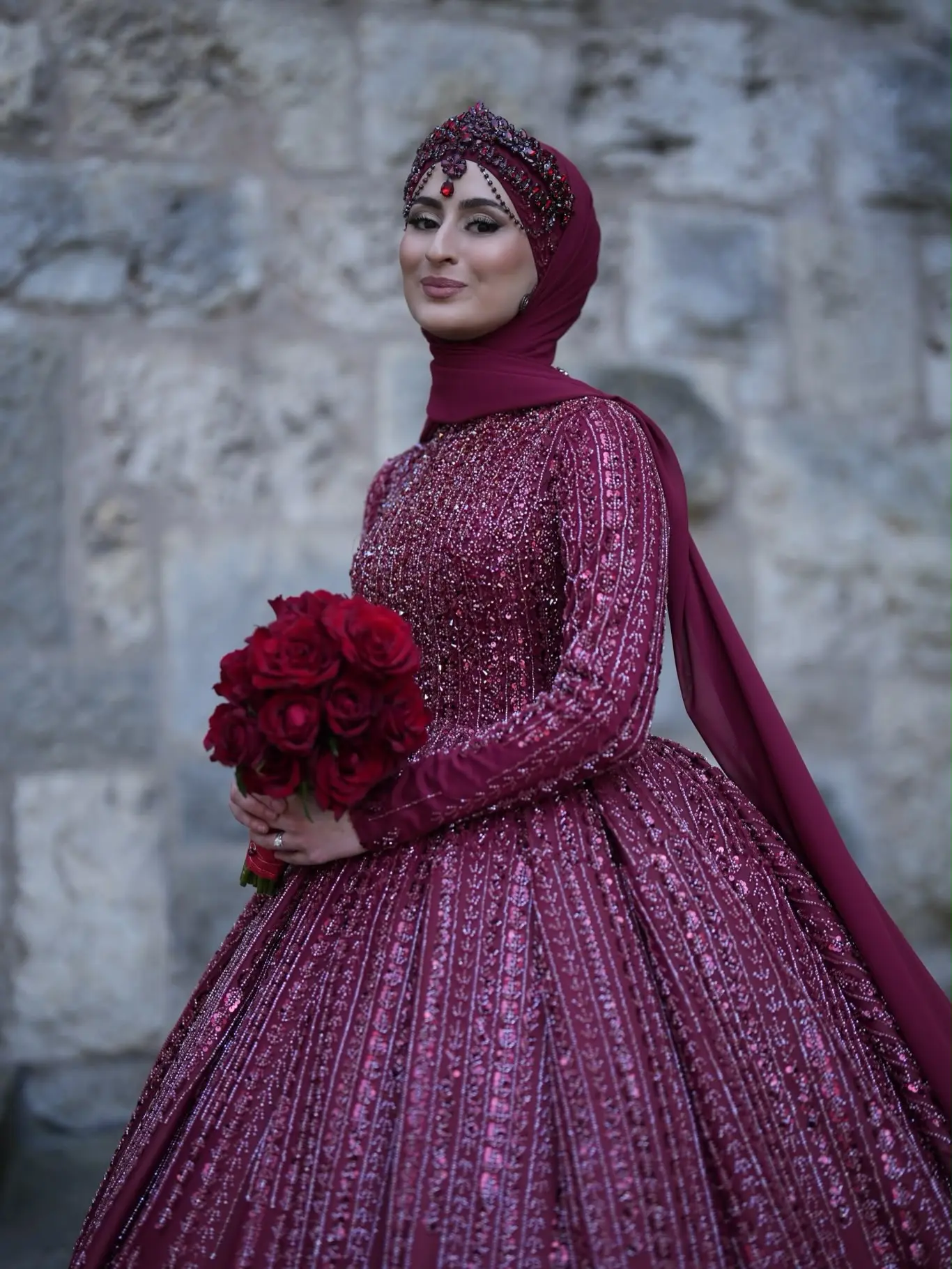 Braut im bestickten burgunderroten Kleid mit passend drapiertem Hijab und Kopfschmuck