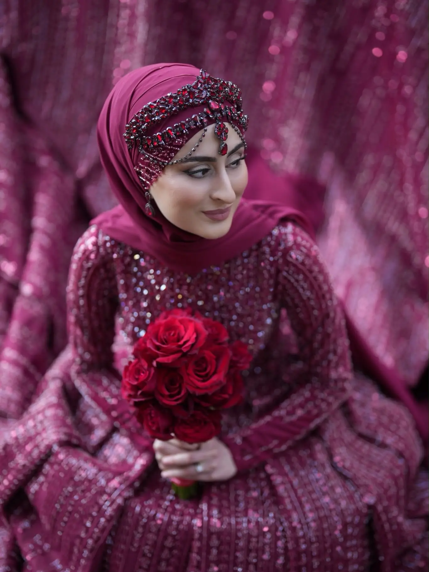 Sitzende Braut mit burgunderrotem Hijab, Kopfschmuck und Rosenstrauß