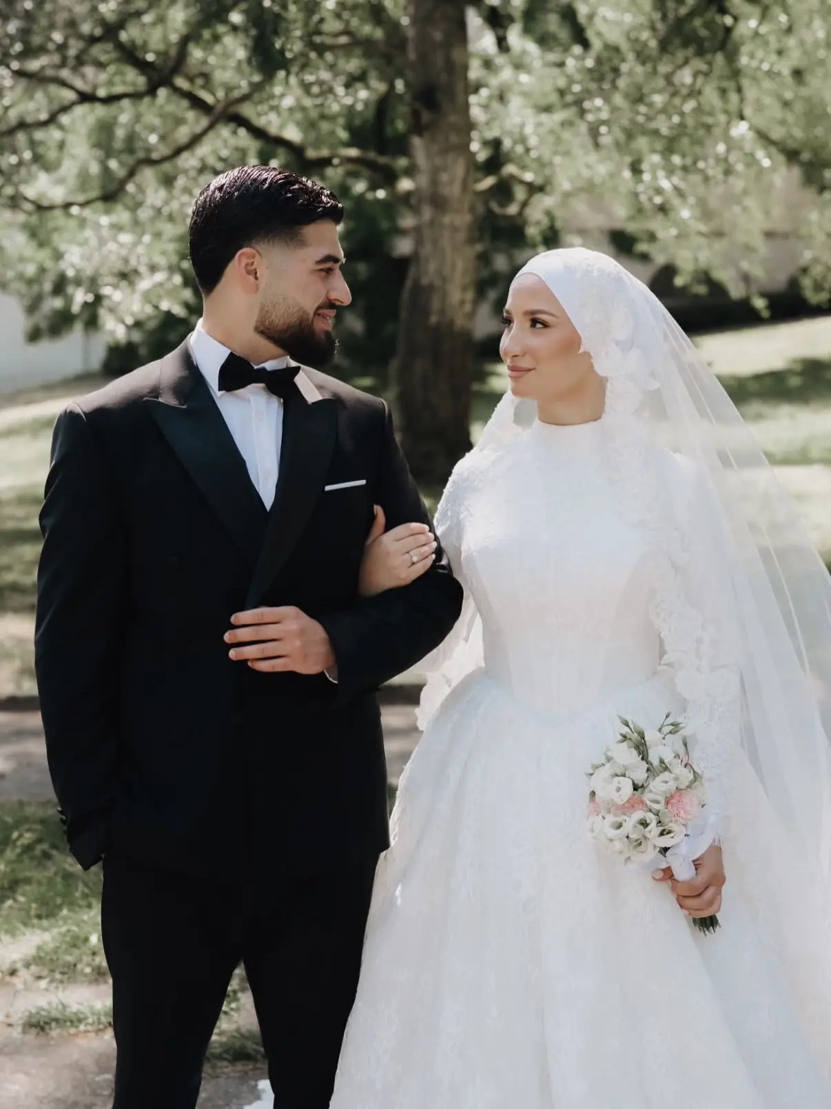 Brautpaar Arm in Arm im Park, Braut mit weißem Hijab und langem Schleier