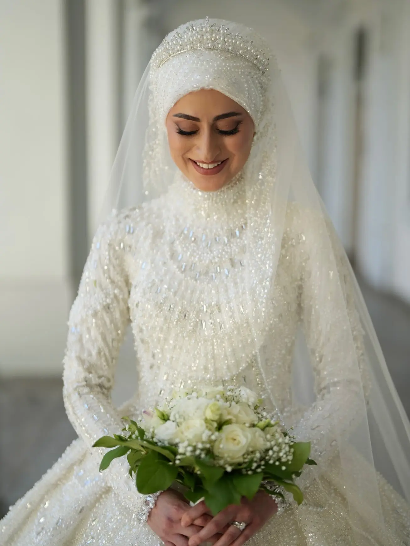 Lächelnde Braut mit weißem Perlen-Hijab, Schleier und Brautstrauß