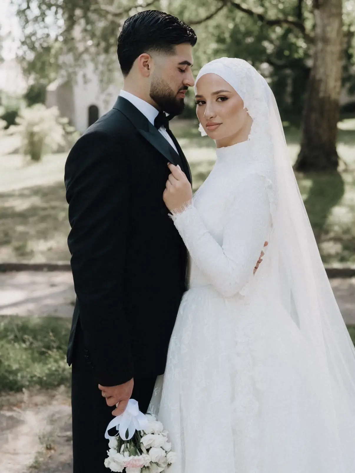 Braut mit weißem Hijab und Spitzenschleier neben dem Bräutigam im Park